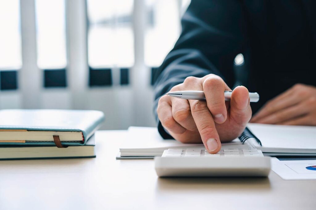 Businessman presses a calculator on a desk with notebooks